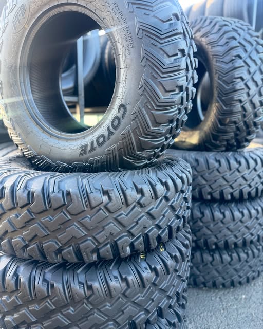 Stacked off-road tires with aggressive mud-terrain tread, one showing its sidewall lettering.