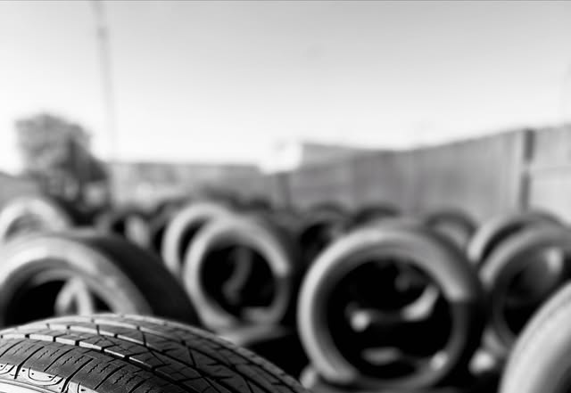 Black and white photo of rows of used tires standing outdoors, with one tread in sharp focus in the foreground.